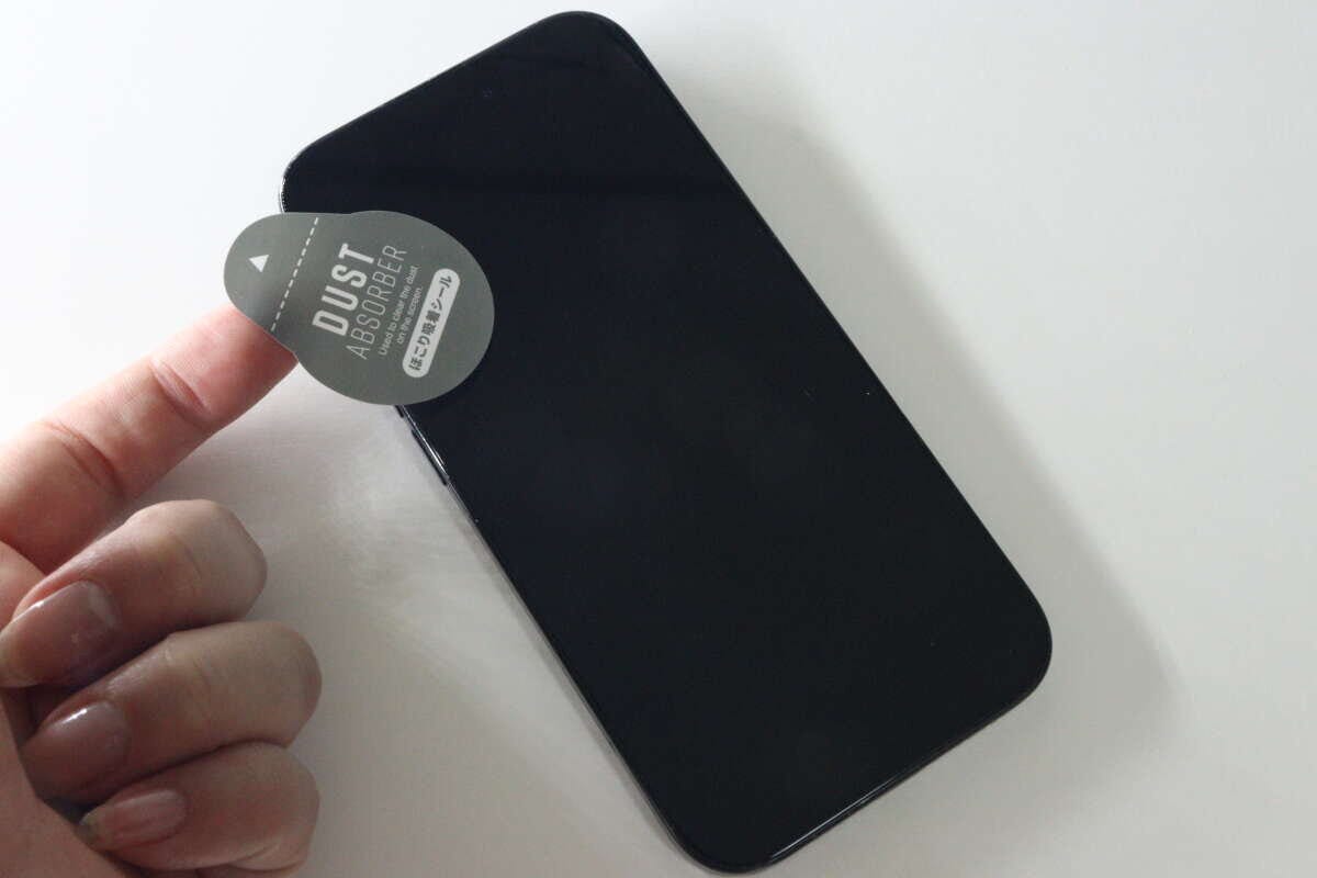 女性の手がホコリ取りシールでスマホ画面のホコリを取っている 女性の手がホコリ取りシールでスマホ画面のホコリを取っている