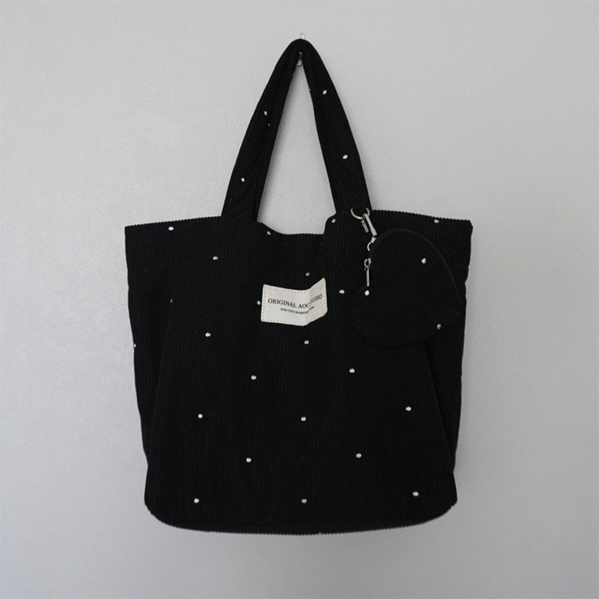 ドット刺繍の黒いトートバッグとハート型ポーチが壁に掛かっている