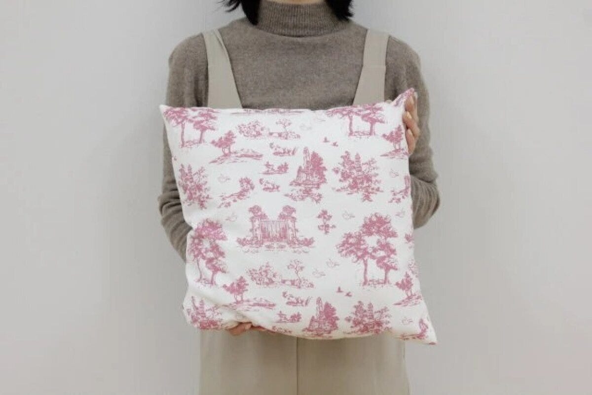 女性が両手でピンク色のトワルドジュイ柄クッションを抱えている