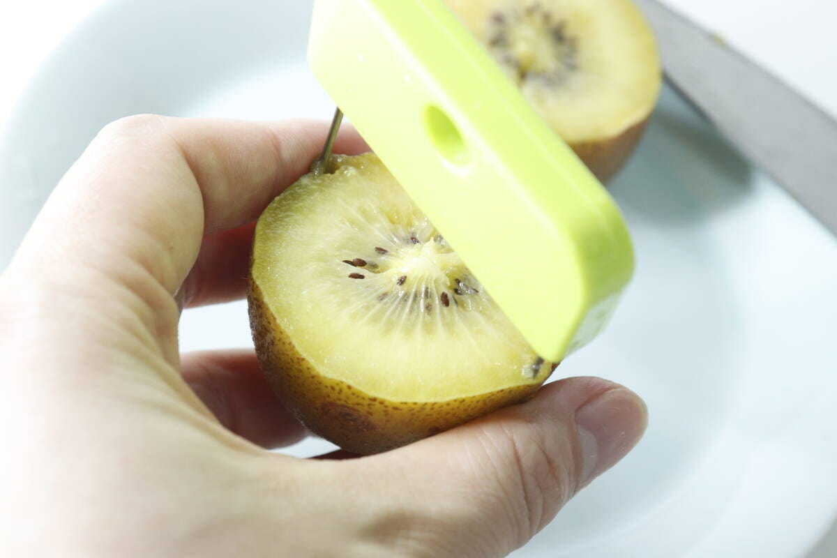半分に切ったキウイに緑色の皮むき器を差し込んでいる手元