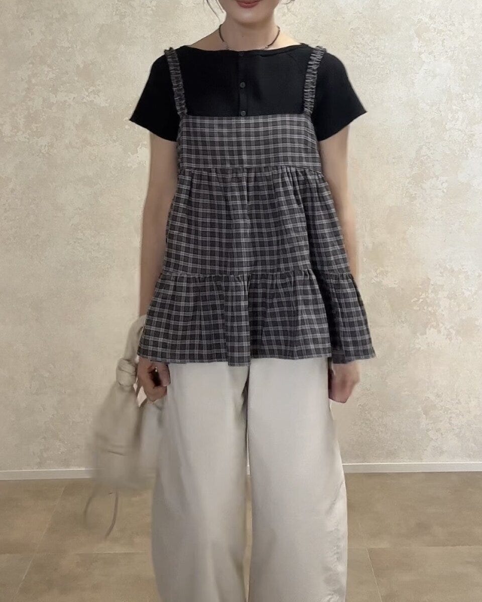 黒Tシャツと白パンツにチェックキャミを重ね着した女性が正面を向いて立っている