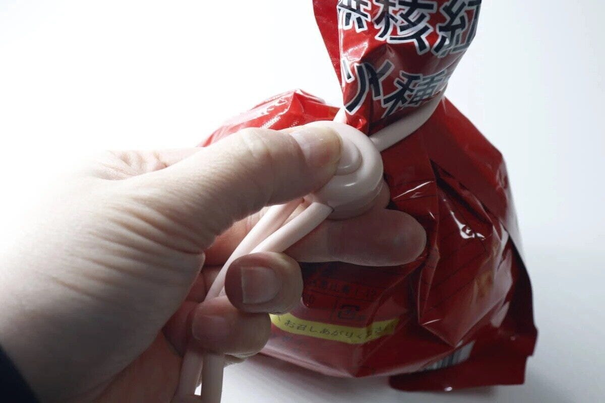 調節できる輪ゴムクリップで赤い袋の口をしっかり留めている手元 調節できる輪ゴムクリップで赤い袋の口をしっかり留めている手元