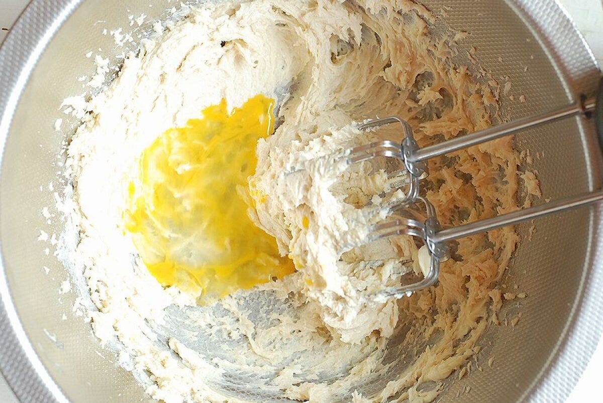 バターと砂糖の生地に溶き卵を加えて泡立て器で混ぜている様子