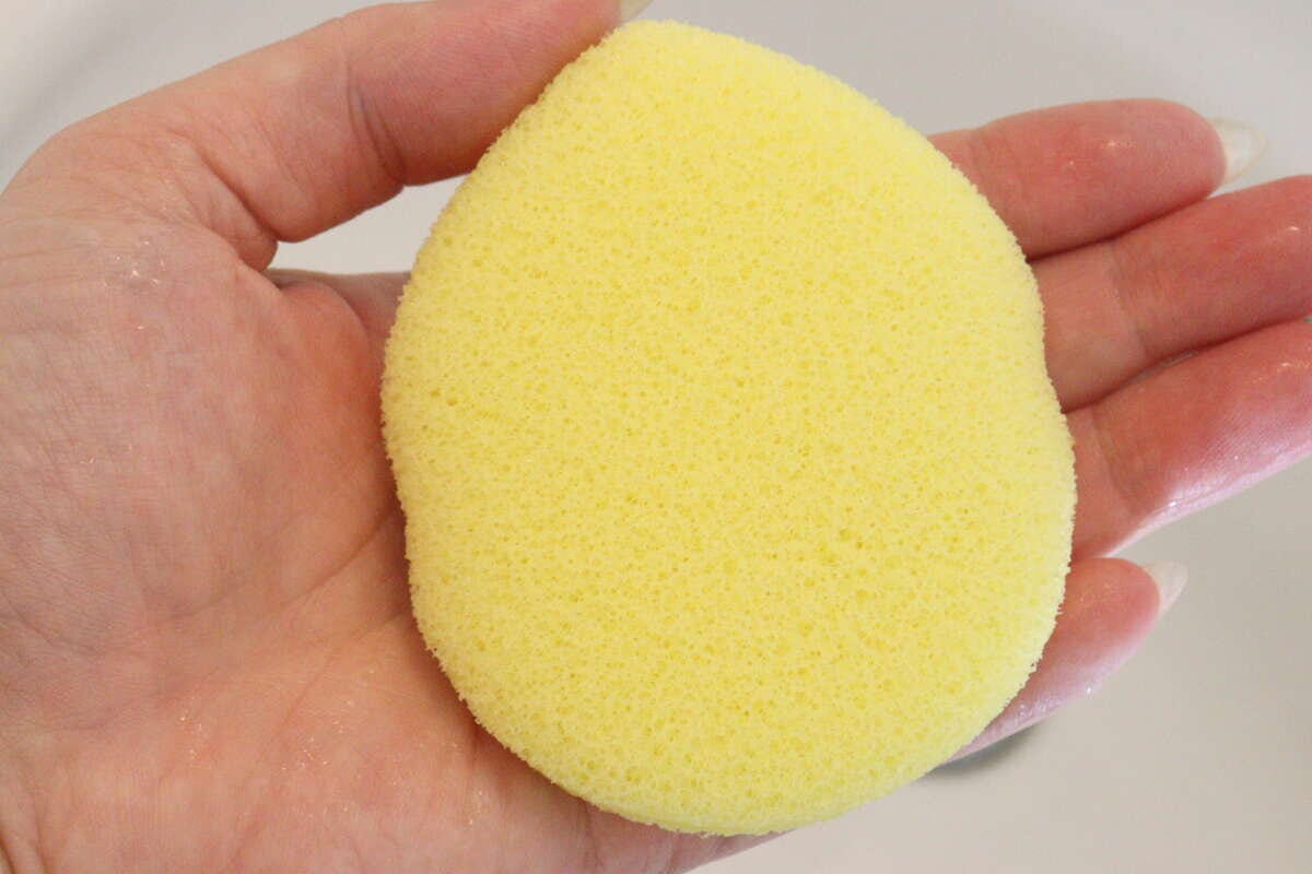 水を含んで膨らんだしずく形の黄色い洗顔パフを手のひらに乗せている