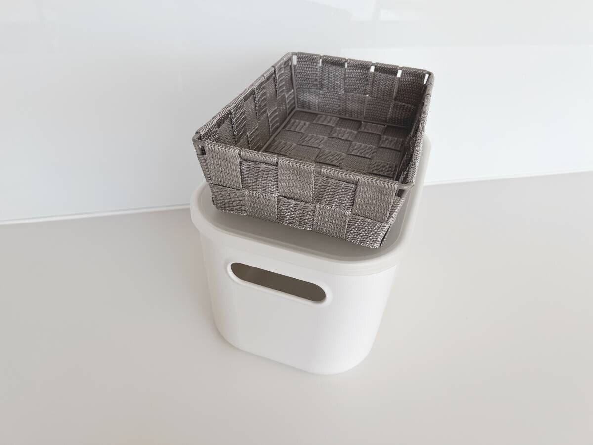 白い収納ボックスの上にグレーの編み込みバスケットが乗っているシンプルな収納アイテムの写真