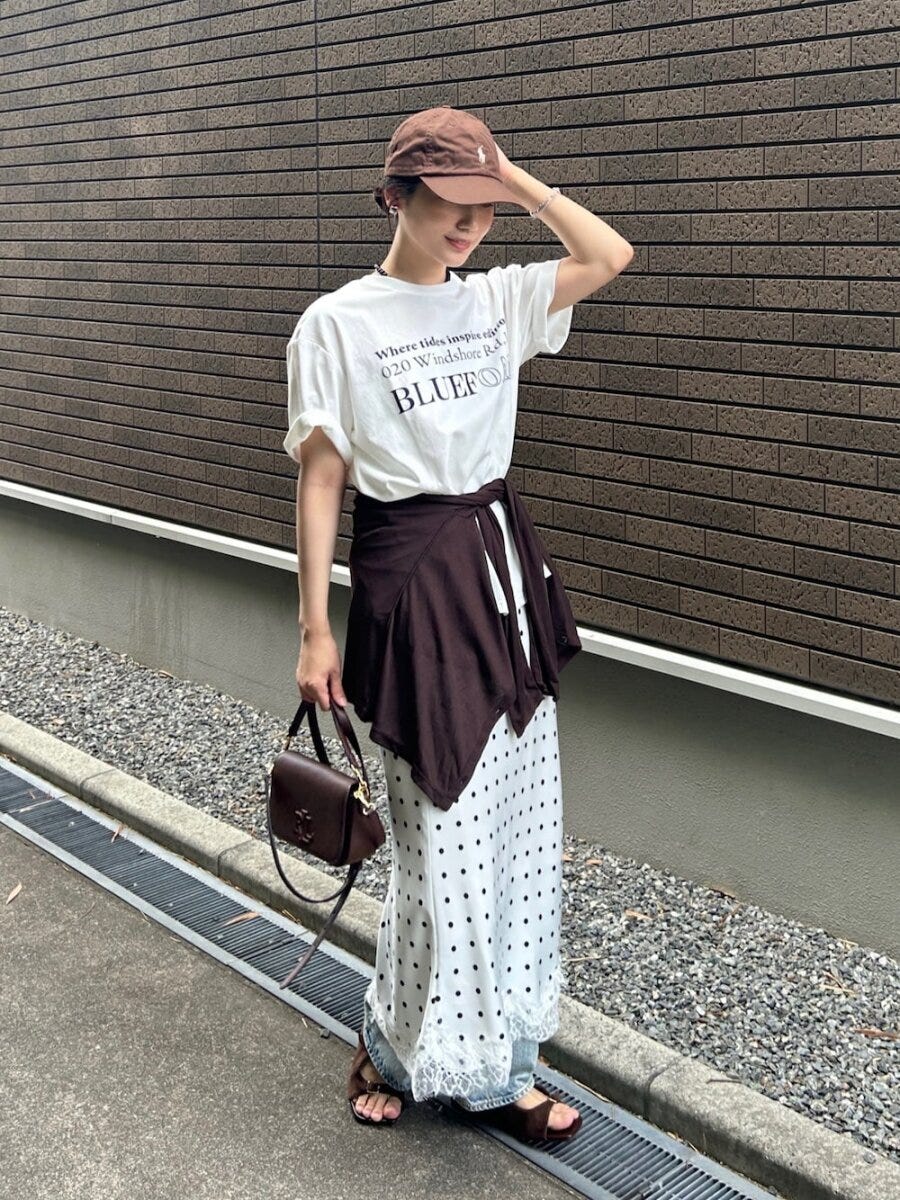 白のロゴTにドット柄スカートとデニムを重ね、茶色のキャップを被る女性 白のロゴTにドット柄スカートとデニムを重ね、茶色のキャップを被る女性