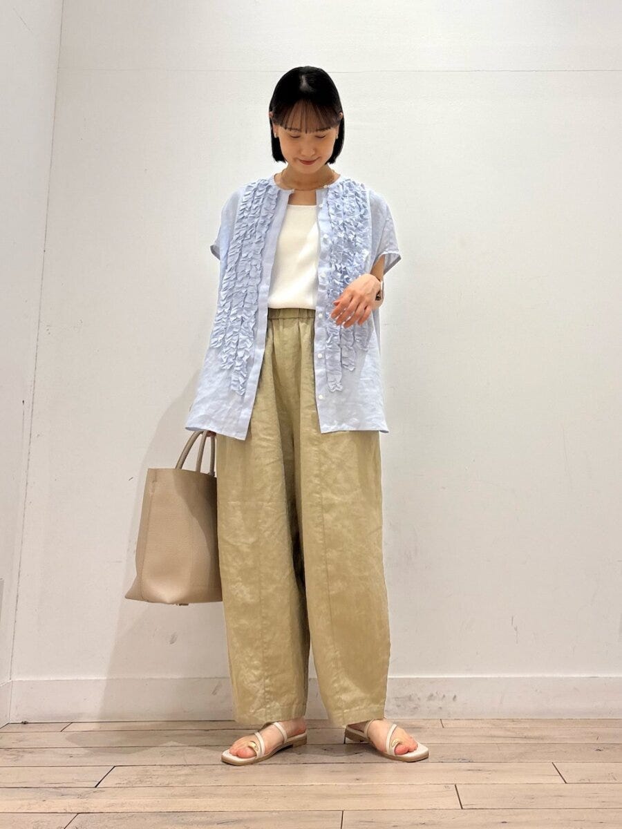 フリル付きブルーシャツとベージュワイドパンツの女性がバッグを持つ