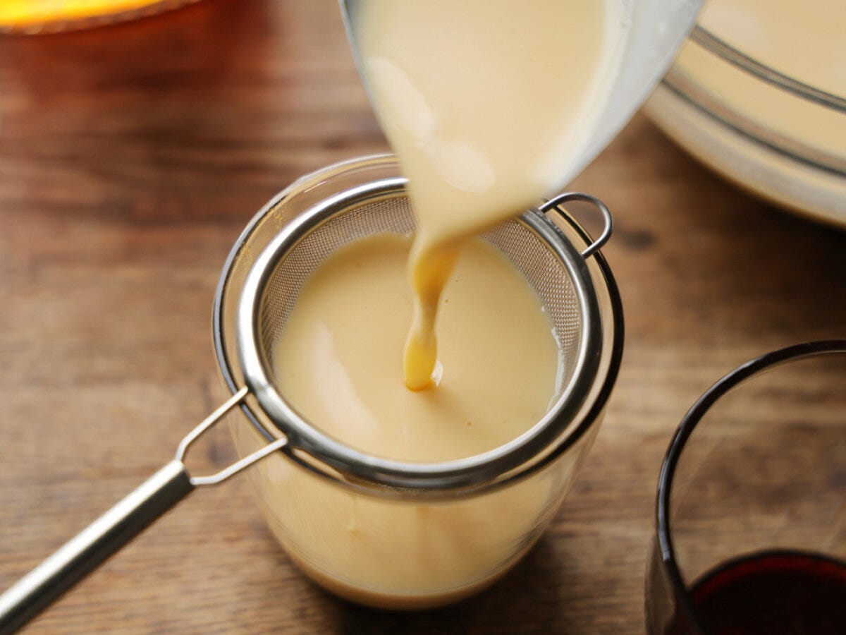 茶こしを使って、なめらかなプリン液を耐熱カップに注ぎ入れている。