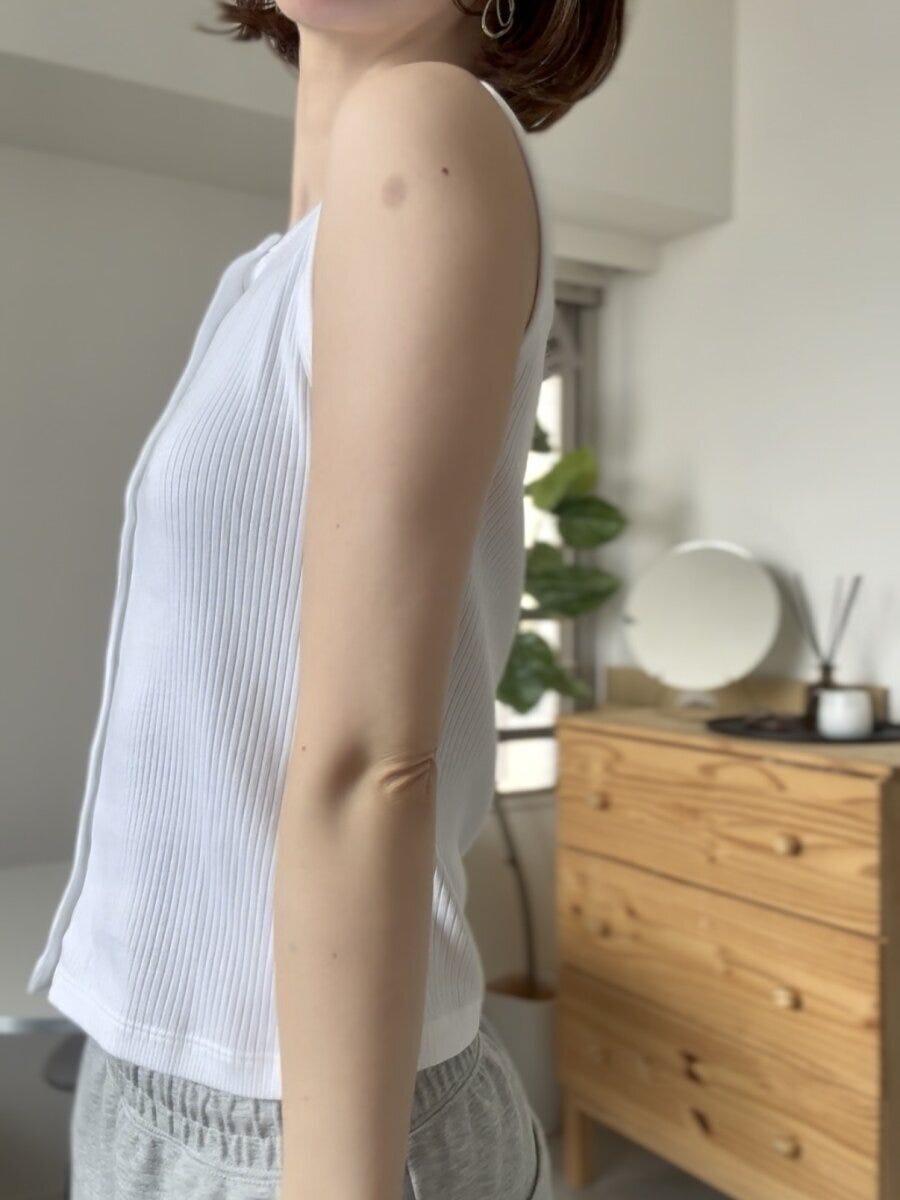 白いリブノースリーブを着た女性が横向きで腕を下ろして立つ全身