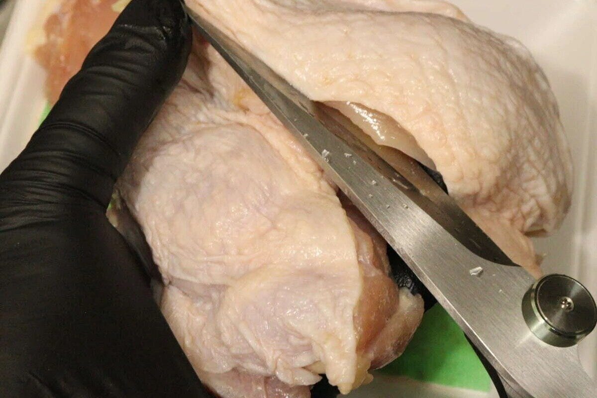 黒い手袋をはめた手がキッチンハサミで鶏肉を切る