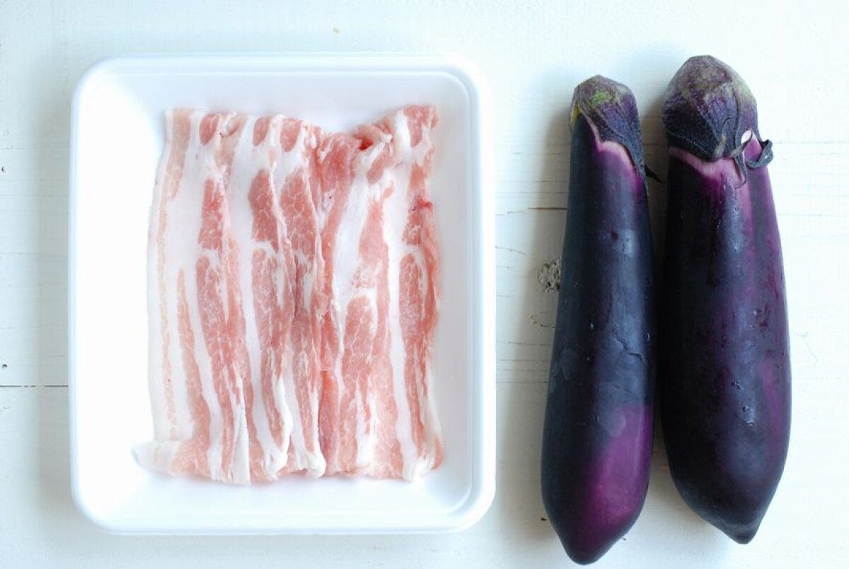 白いトレーに入った豚バラ肉と、隣に並べられた2本のなす