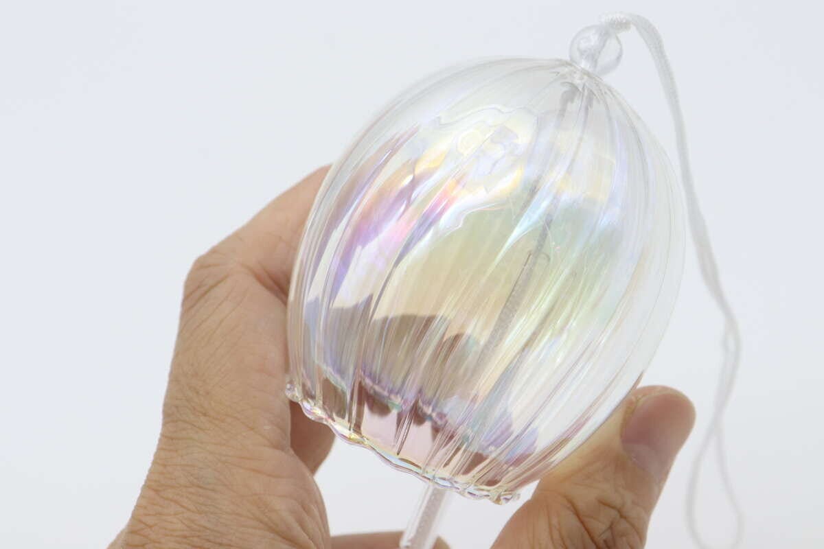 オーロラ加工のガラス風鈴本体を女性の手が持ち、光にかざしている様子 オーロラ加工のガラス風鈴本体を女性の手が持ち、光にかざしている様子
