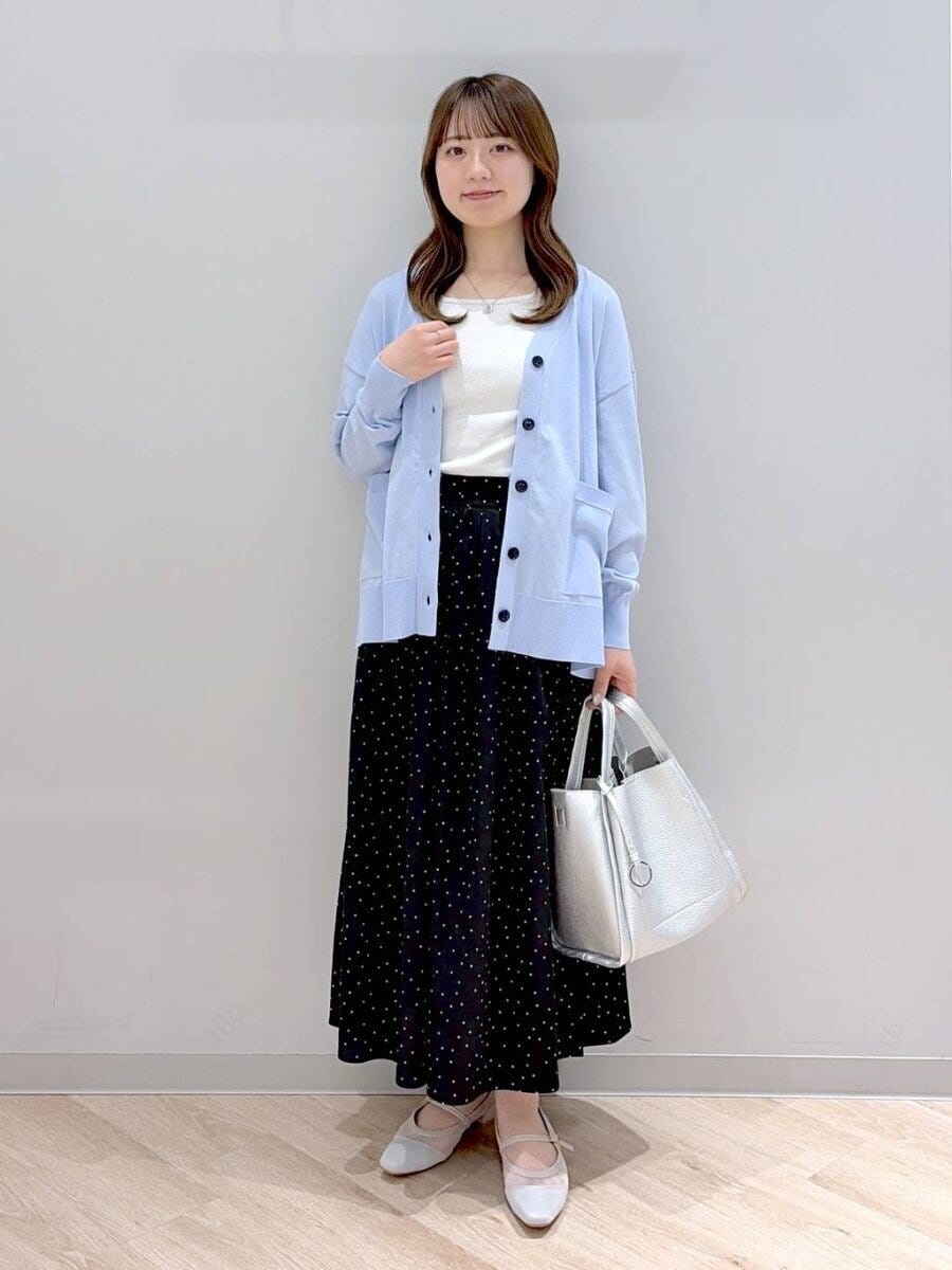水色の長袖カーディガンとドット柄ロングスカートの女性が立っている
