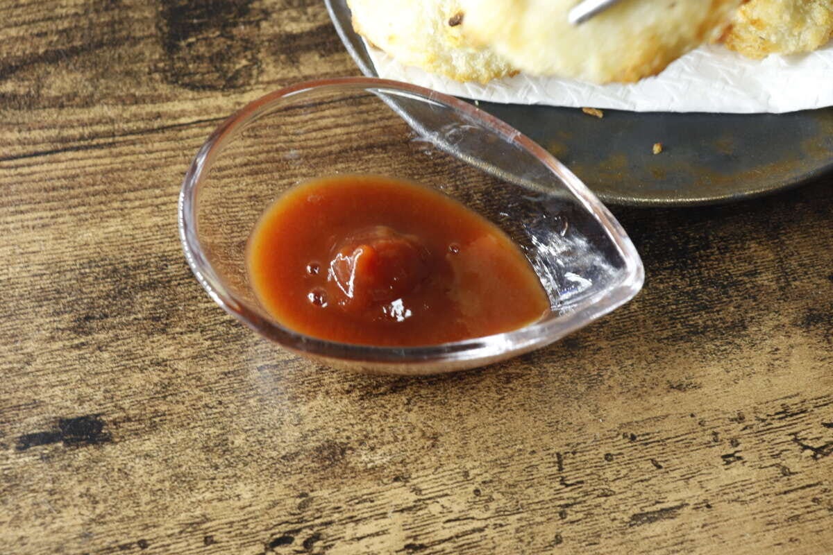 木目のテーブルに置かれた、小皿に入った茶色いトマトケチャップのクローズアップ