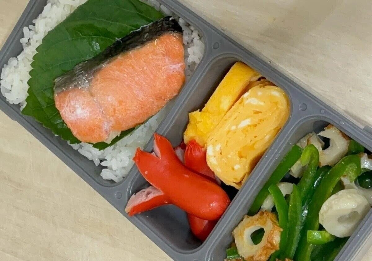 グレーの薄型弁当箱に、ご飯、焼き鮭、卵焼き、ウインナー、ピーマンとちくわの炒め物などのおかずが詰められている グレーの薄型弁当箱に、ご飯、焼き鮭、卵焼き、ウインナー、ピーマンとちくわの炒め物などのおかずが詰められている