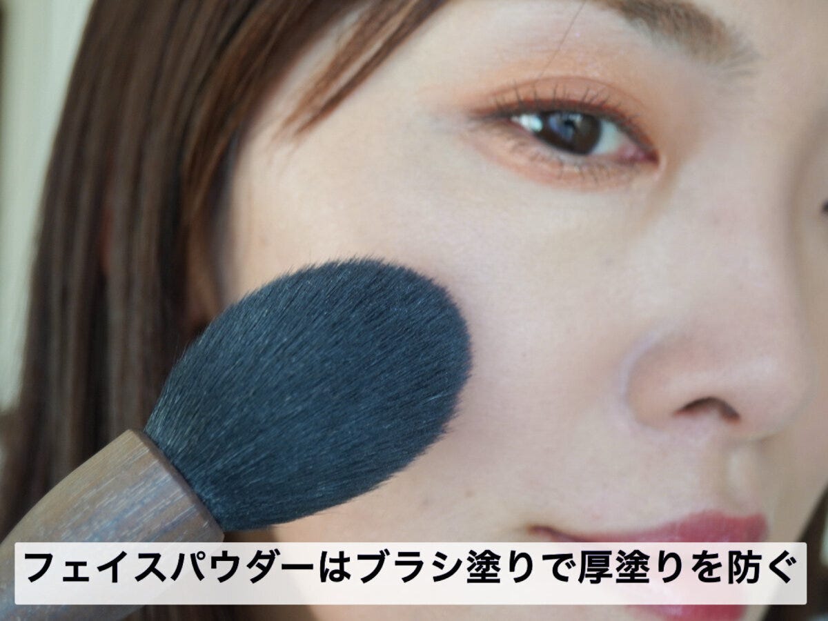 フェイスパウダーをブラシで頬に塗る女性 フェイスパウダーをブラシで頬に塗る女性