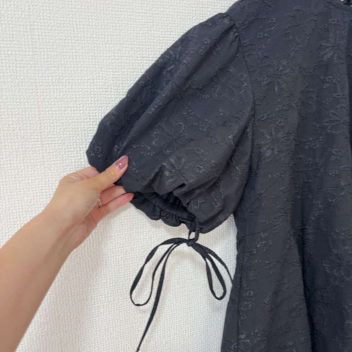 黒いバルーンスリーブチュニックの袖とリボンを指でつまんでいる 黒いバルーンスリーブチュニックの袖とリボンを指でつまんでいる