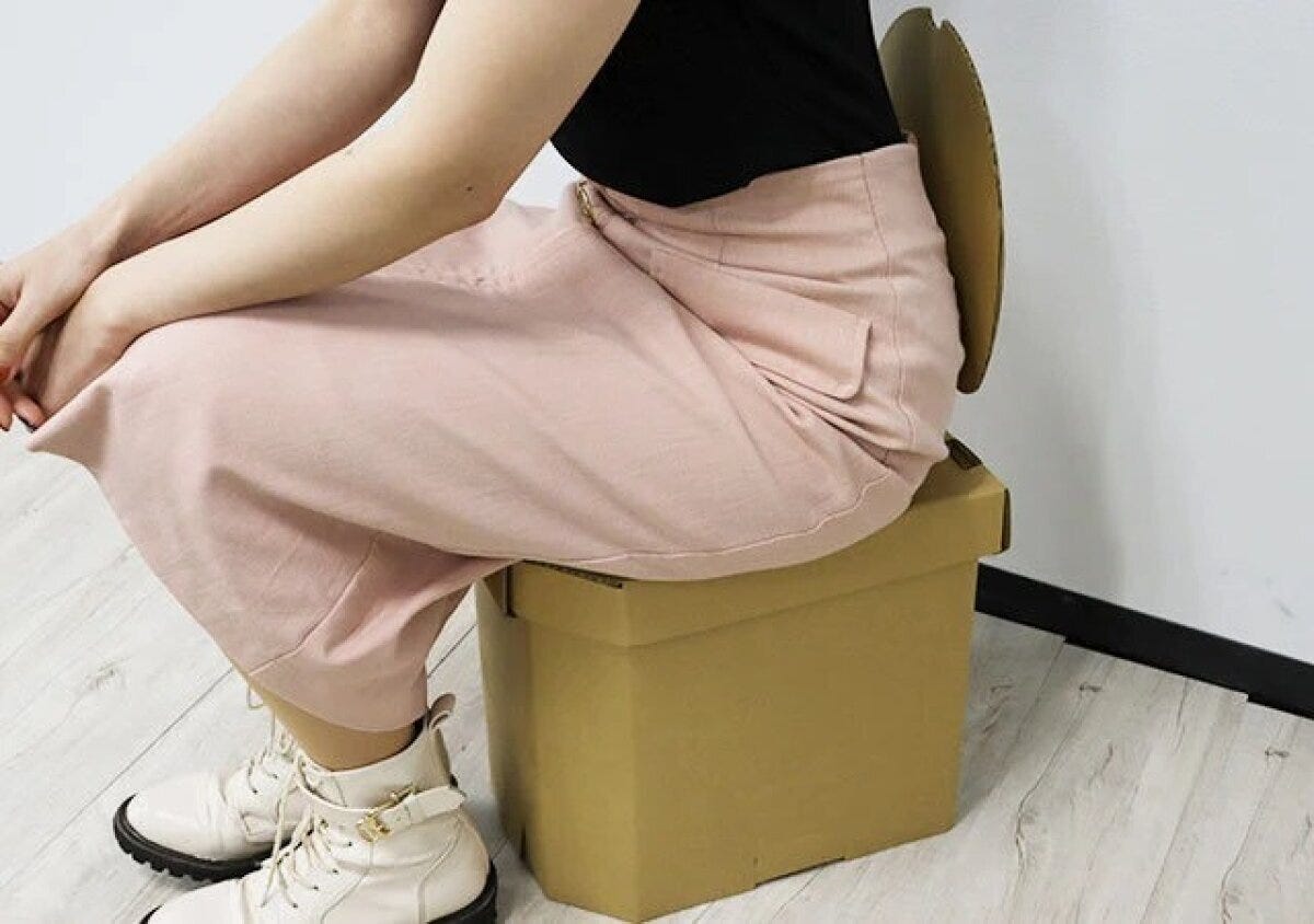 女性が組み立てられた茶色い段ボール製簡易トイレに座っている横からの写真