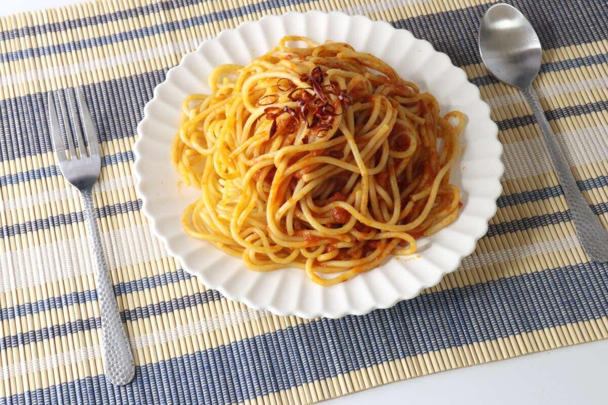トマトソースのパスタが盛られた白い皿の左右に槌目風スプーンとフォークが置かれている