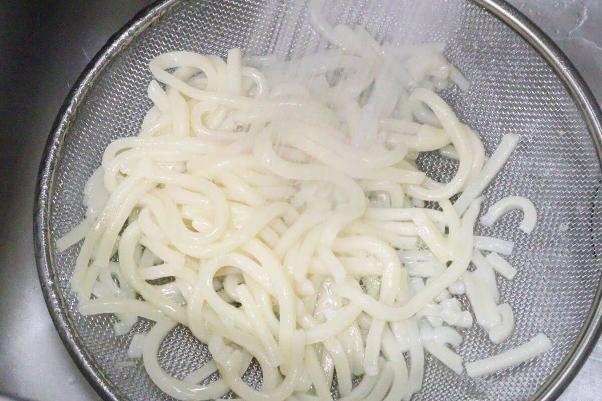 ステンレス製の浅型ザルでうどんを湯切りしている様子