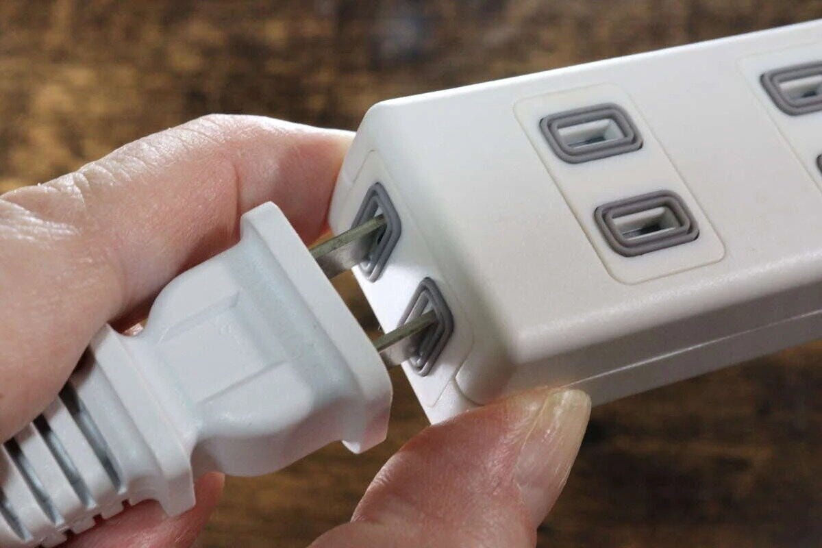 手が白い電源タップの差し込み口に、プラグを差し込もうとしている