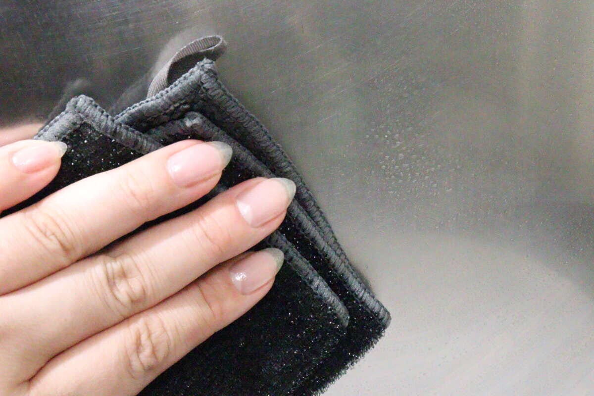女性の手がマイクロファイバークロスでコンロの油汚れを拭いている