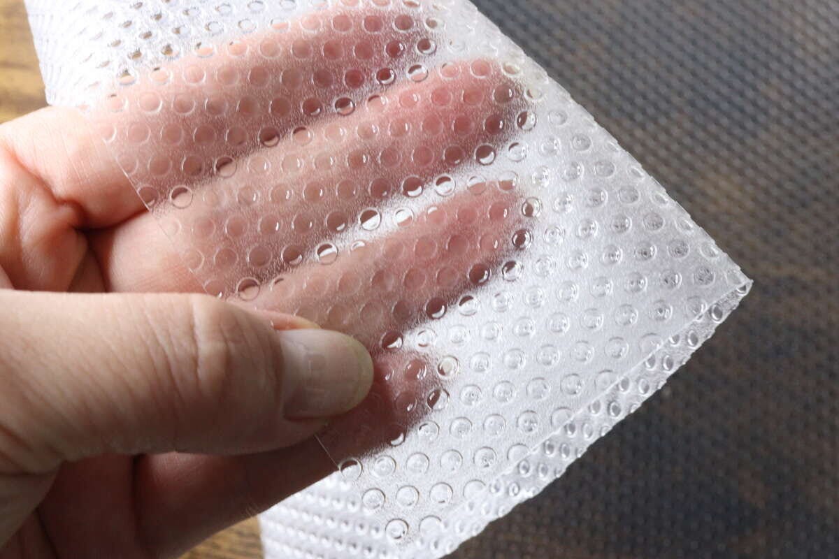 手で冷蔵庫マットを持ち、透明度と凹凸加工を確認している様子