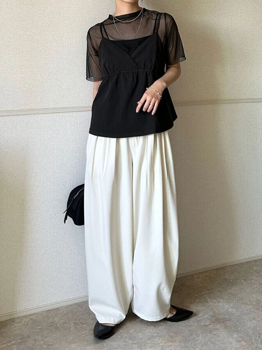 黒いシアーTとキャミソール、白いワイドパンツを着用した女性の全身