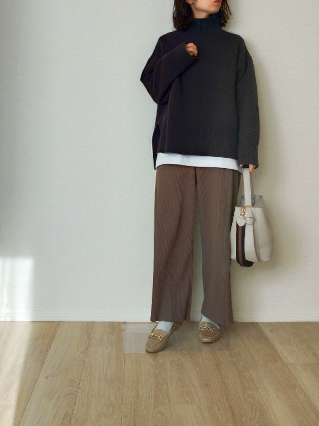 白のロンTに黒のハイネックニットをレイヤードし、ブラウンのワイドパンツとベージュローファー、白のハンドバッグをコーディネート