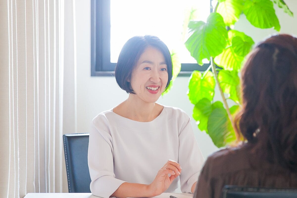 白いトップスの女性がテーブル越しにクライアントと向き合い笑顔で話している様子