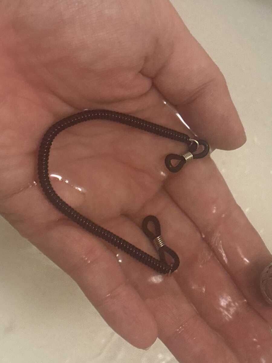 手のひらに乗せた黒いメガネストラップを水で洗っている様子