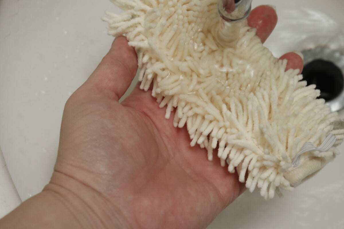 流水で白いハンディモップの汚れを洗い流している手元 流水で白いハンディモップの汚れを洗い流している手元