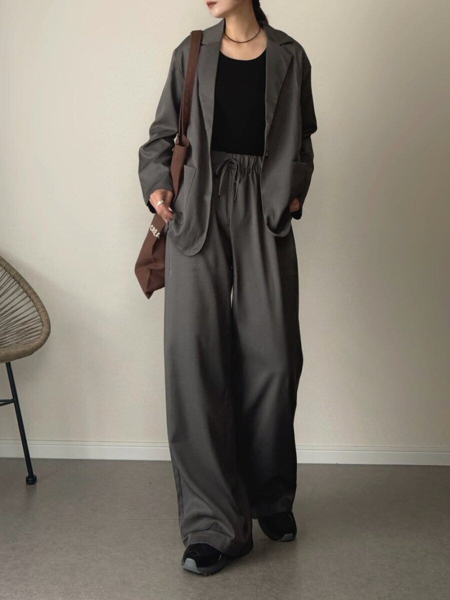 グレーのジャケットとワイドパンツを着て黒いインナーとスニーカーを合わせた女性