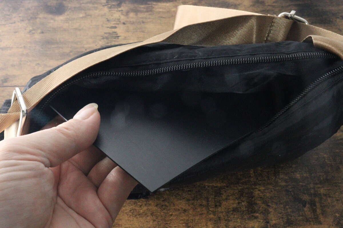 女性の手がカットした黒いプラ底板をバッグの底に入れている 女性の手がカットした黒いプラ底板をバッグの底に入れている
