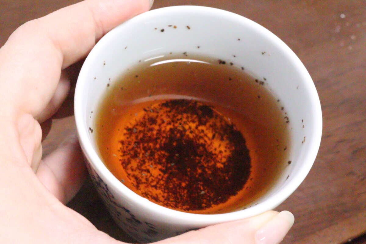 抽出後の紅茶が入ったカップを女性の指が持っており、細かい茶葉が底に沈んでいる 抽出後の紅茶が入ったカップを女性の指が持っており、細かい茶葉が底に沈んでいる