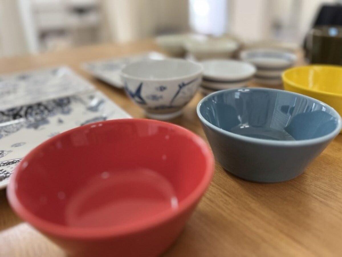 木製のテーブルに並べた赤・水色・黄色のボウルと、藍色の絵付けの和茶碗、白い小皿を仕分けている様子