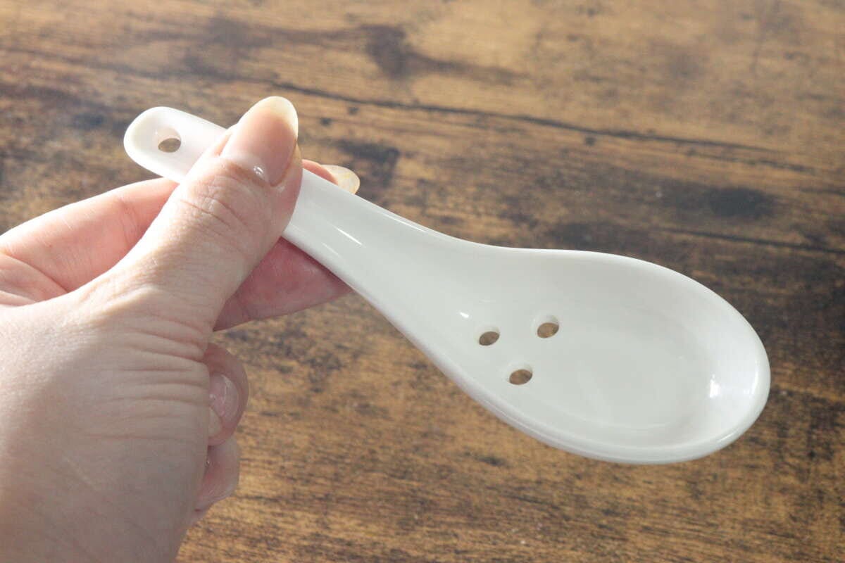 女性の指が白い陶器製の穴あきレンゲを横から持っている