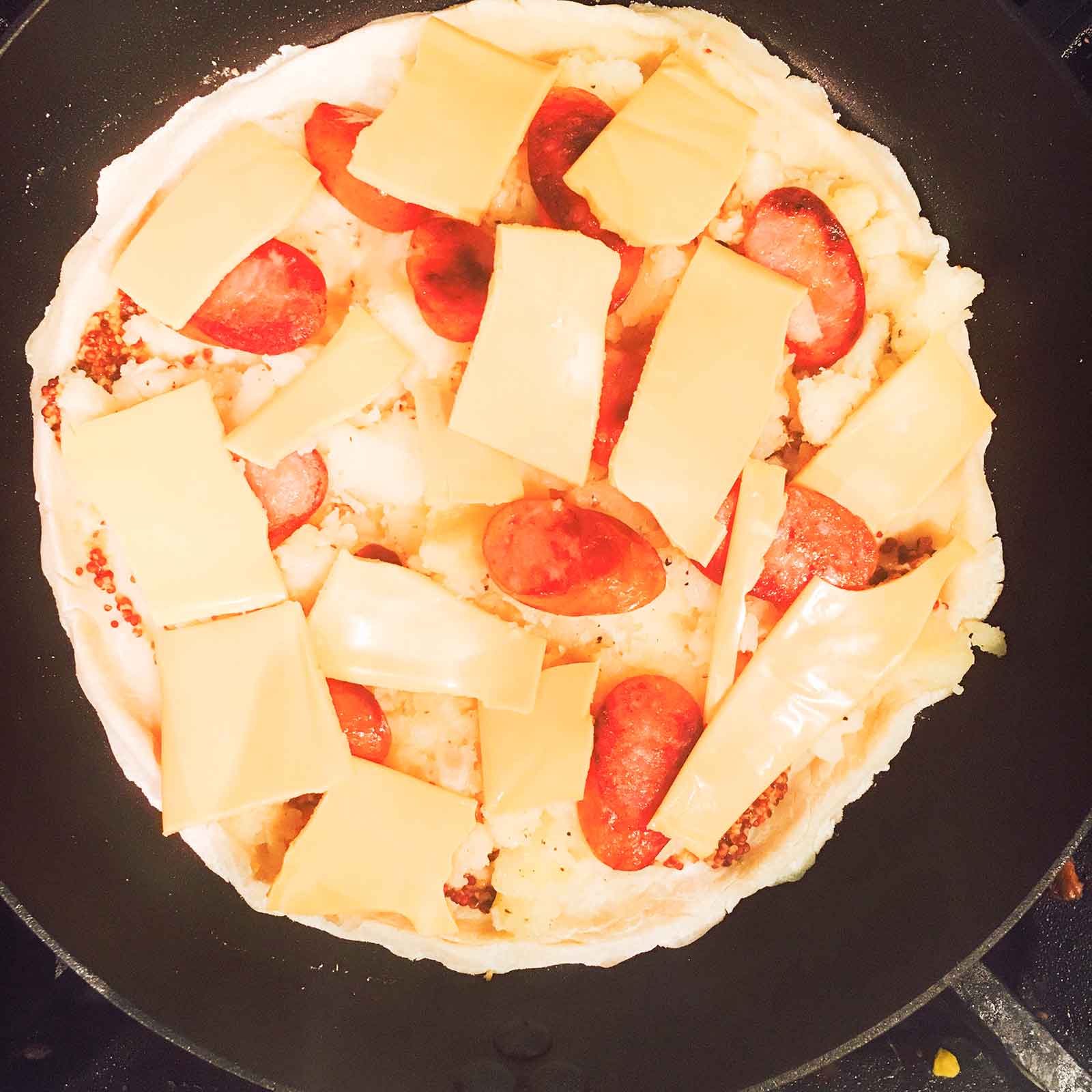 手順6：潰したじゃがいも、ウインナー、チェダーチーズをのせ蓋をし弱火で10分～焼く／画像提供：柏原歩