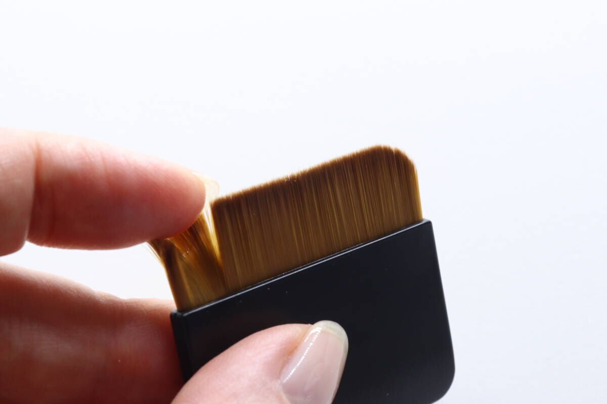 女性が薄型ファンデーションブラシの毛先を指で触っている