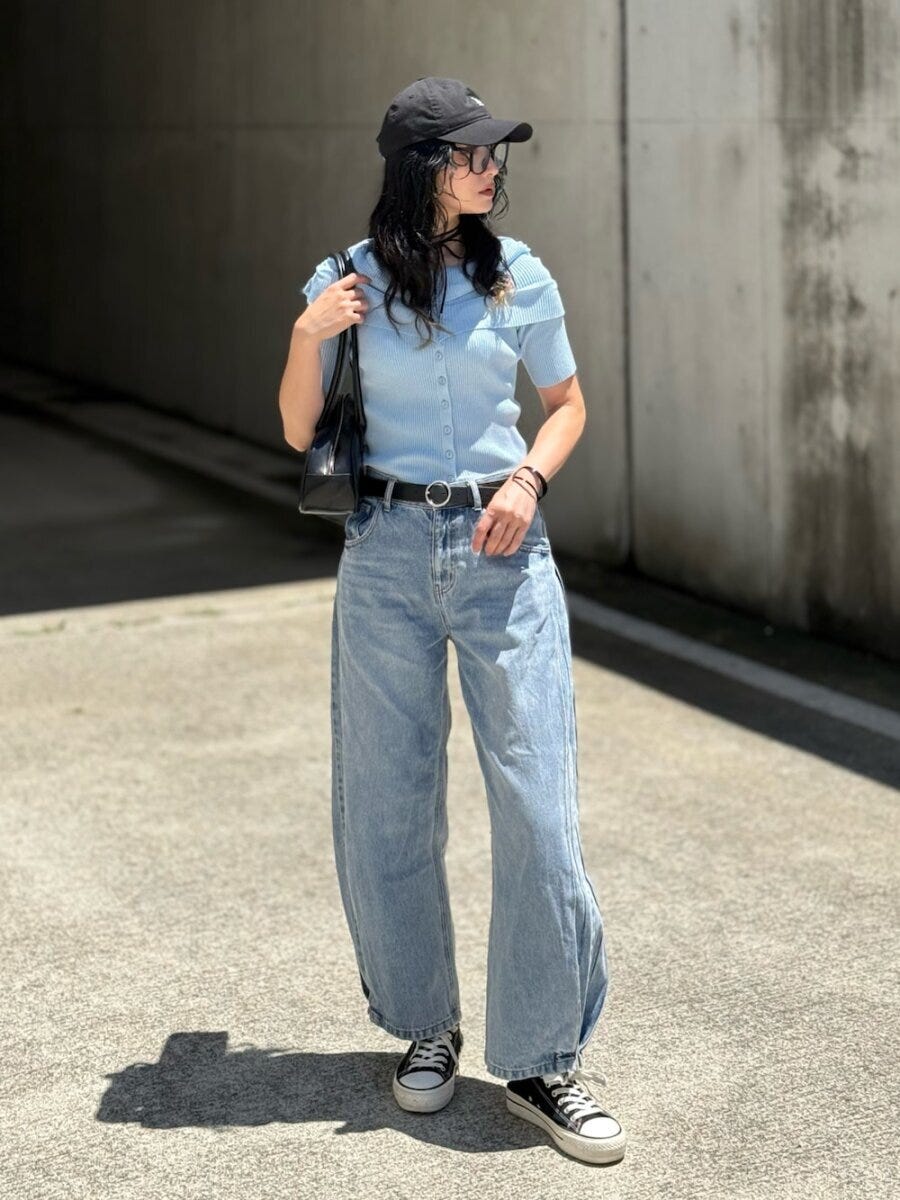 黒いキャップと水色のカーディガン、ライトブルーのワイドデニムを着用した女性が横を向いて立っている