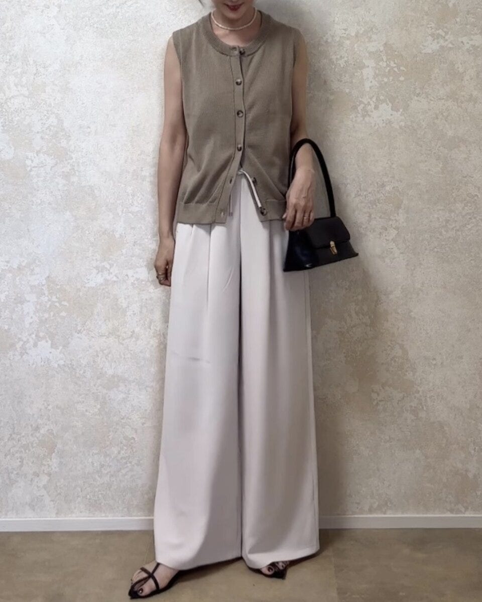 ベージュのノースリーブカーディガンと白いワイドパンツを着用した女性