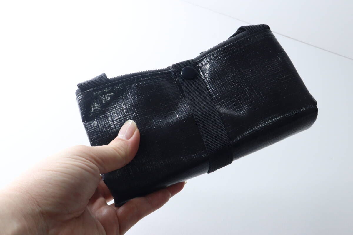 女性の手が、コンパクトに折りたたまれた黒いトートバッグを持つ