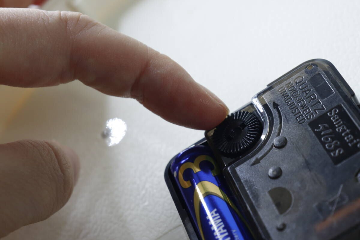 ダイソー掛け時計の裏面。電池を入れ時刻合わせダイヤルを回す指
