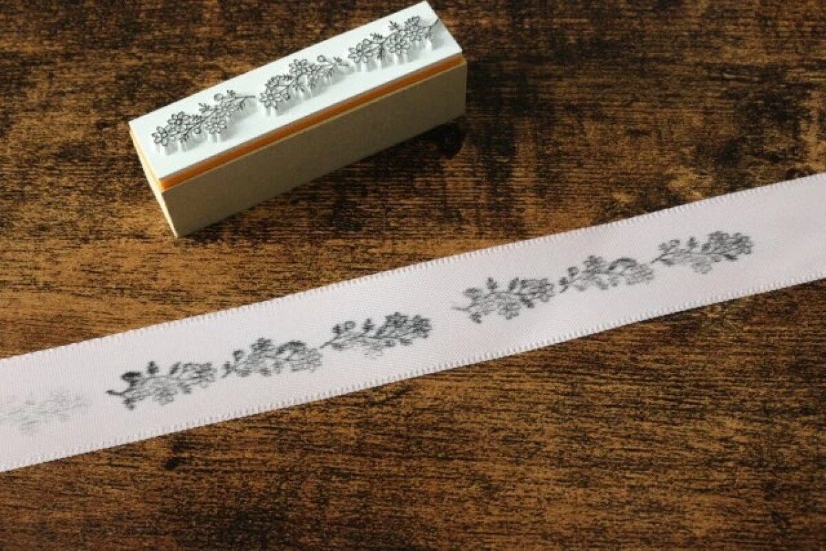 ボタニカル柄のスタンプで白いリボンに模様が押されている様子 ボタニカル柄のスタンプで白いリボンに模様が押されている様子