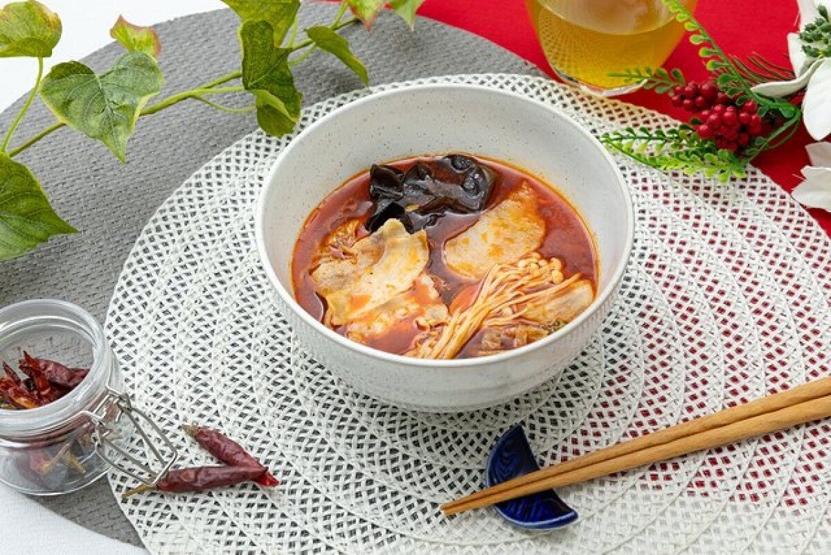 白い器に盛り付けられた旨辛火鍋と箸が食卓に置かれている 白い器に盛り付けられた旨辛火鍋と箸が食卓に置かれている