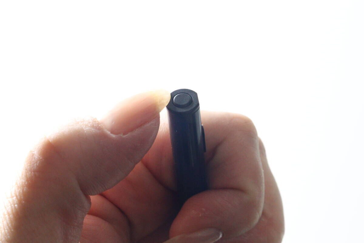 女性の指が充電式タッチペンの上部にある電源ボタンを押しているクローズアップ
