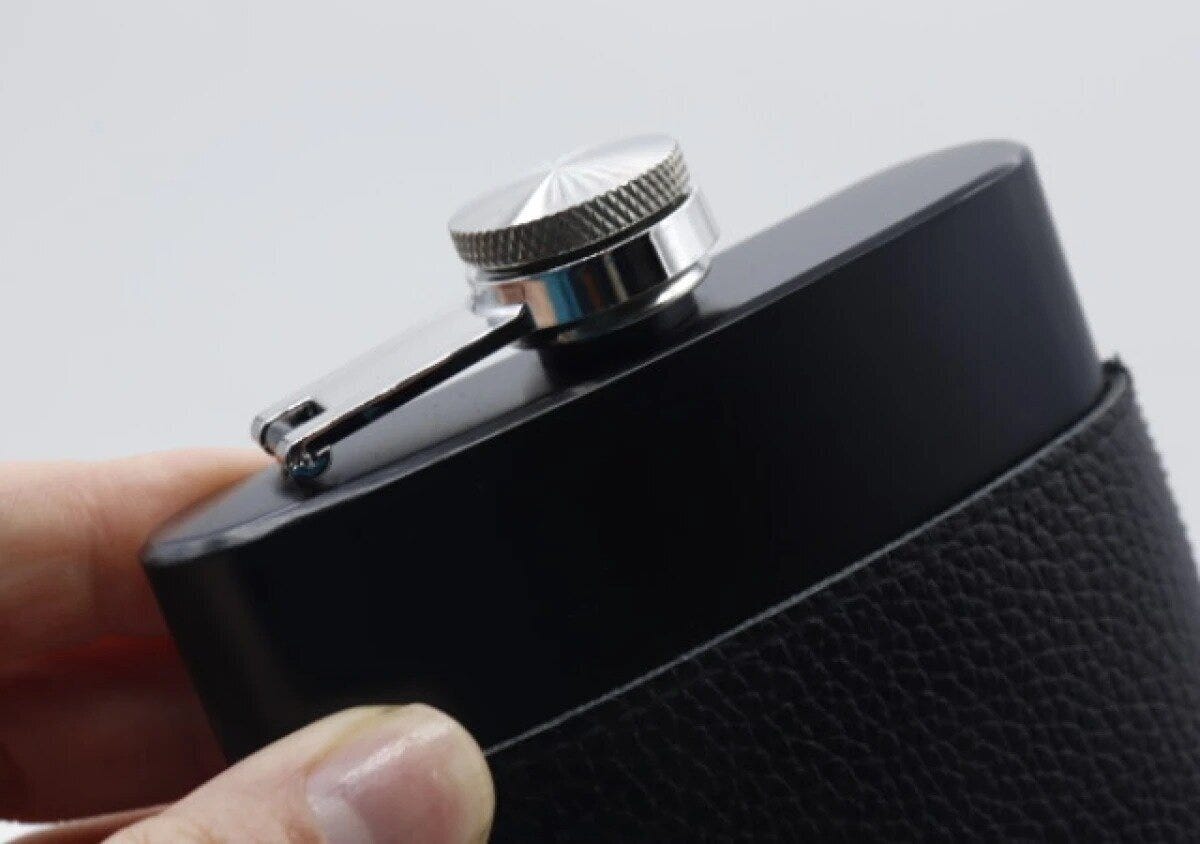 手が黒いスキットルを革製カバーに差し込んでいる様子
