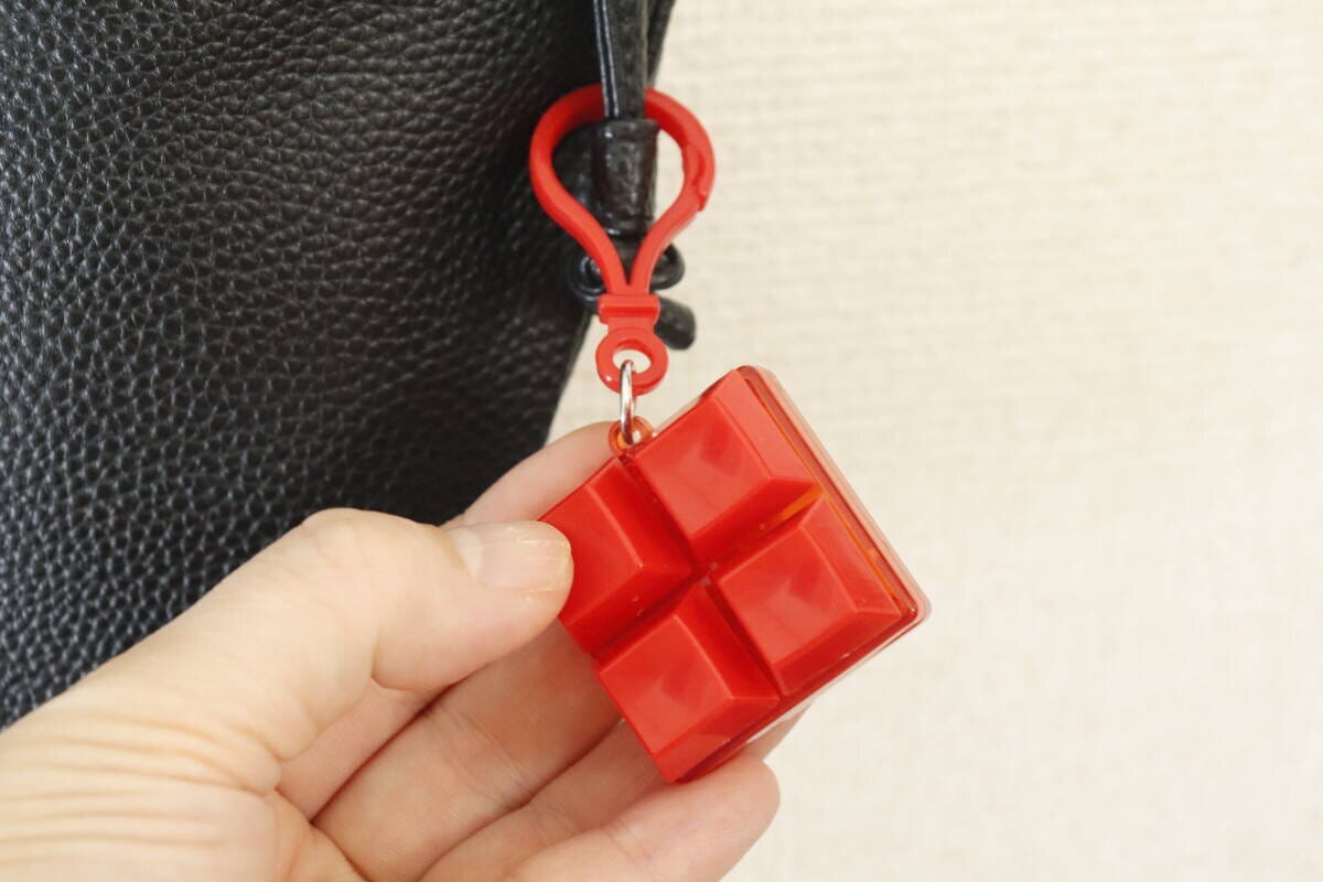 黒いバッグに付けられた赤いキーホルダーを指でつまんで見ている 黒いバッグに付けられた赤いキーホルダーを指でつまんで見ている