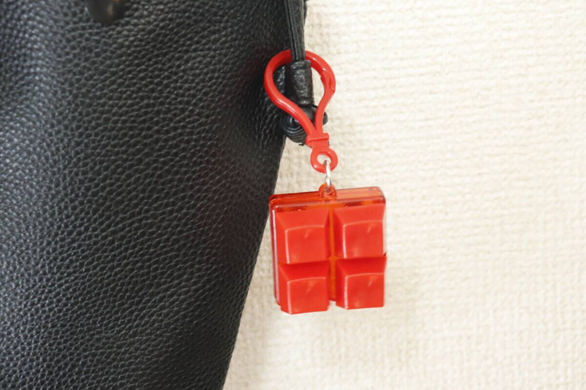 黒いバッグの持ち手に赤いカラーブロックキーホルダーがぶら下がっている 黒いバッグの持ち手に赤いカラーブロックキーホルダーがぶら下がっている