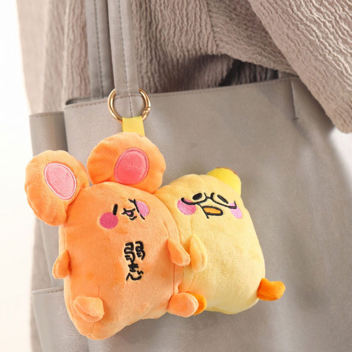 オレンジと黄色のキャラクターぬいぐるみチャームがグレーのバッグに付いている